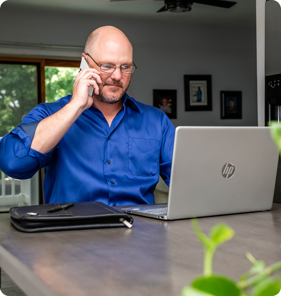 Man in blue shirt using laptop and phone.